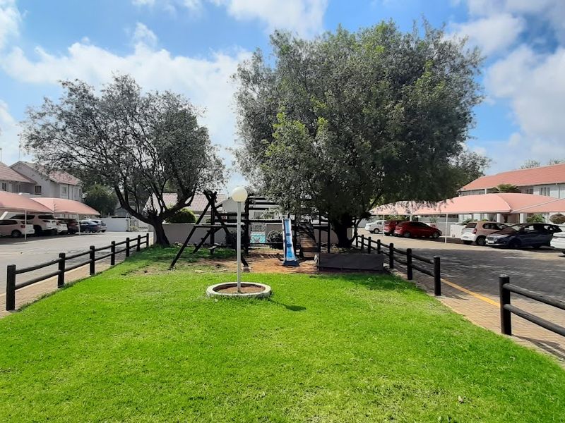 A well-maintained communal garden area featuring paved parking bays with shade-cloth carports and established trees within a townhouse complex.