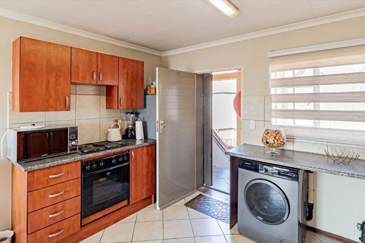 Functional kitchen featuring wood-finish cabinetry, granite countertops, built-in oven and hob, with dedicated space for a washing machine and direct exterior access.