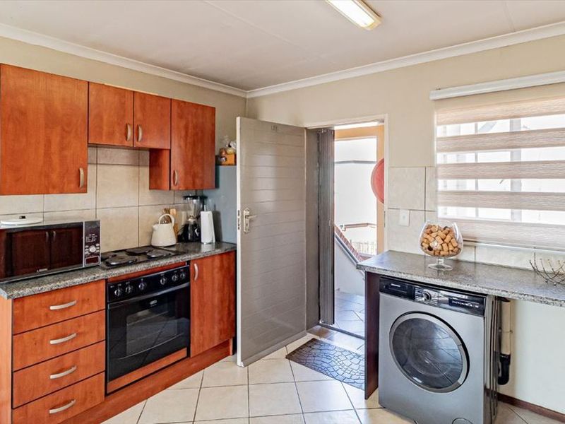 Functional kitchen featuring wood-finish cabinetry, granite countertops, built-in oven and hob, with dedicated space for a washing machine and direct exterior access.