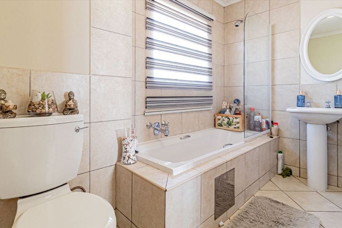 A well-maintained bathroom featuring a pedestal basin, a built-in bathtub with a glass shower screen, and neutral ceramic tiling throughout.