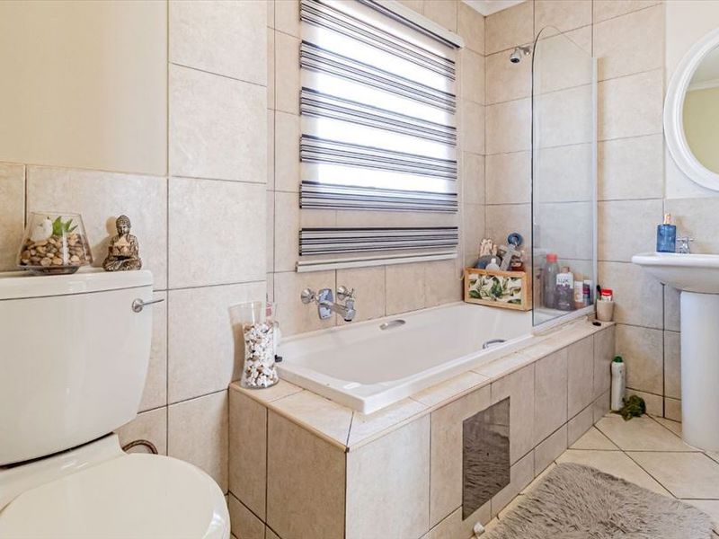 A well-maintained bathroom featuring a pedestal basin, a built-in bathtub with a glass shower screen, and neutral ceramic tiling throughout.