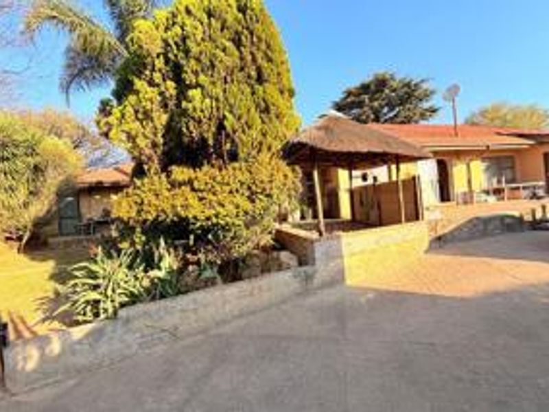 Front exterior view of the property featuring a paved driveway, a thatched lapa, and established garden landscaping.