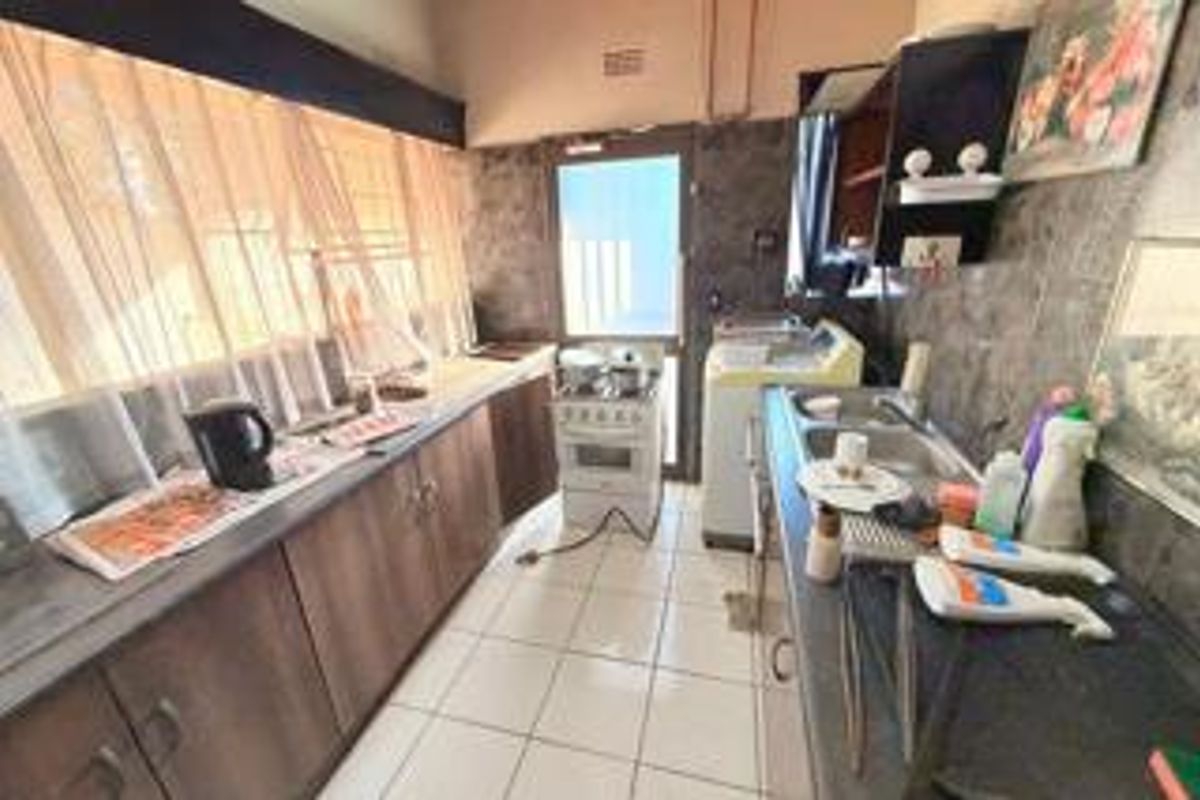 A functional kitchen featuring built-in cabinetry, a gas stove, and double sink with tiled finishes, offering potential for modernization.