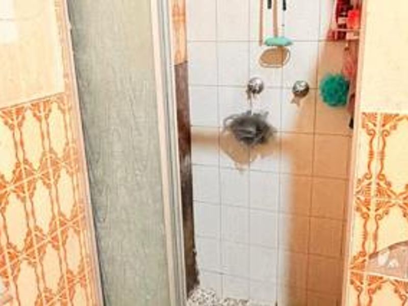 A dated bathroom shower area featuring original patterned wall tiles and a standard shower enclosure, showing signs of wear and tile damage.