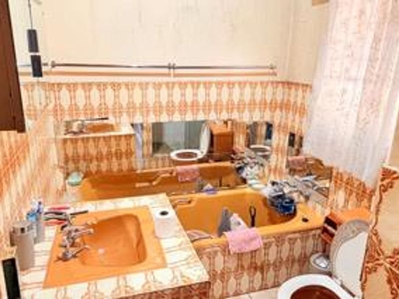 A dated bathroom featuring built-in vanity, bathtub, and toilet with original patterned wall tiling throughout.