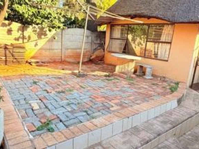 Rear exterior area featuring a thatched roof structure, paved patio space, and perimeter walling, requiring maintenance and landscaping to improve the outdoor living area.