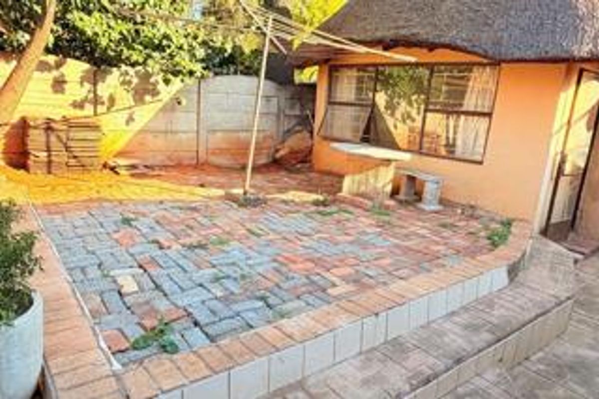 Rear exterior area featuring a thatched roof structure, paved patio space, and perimeter walling, requiring maintenance and landscaping to improve the outdoor living area.