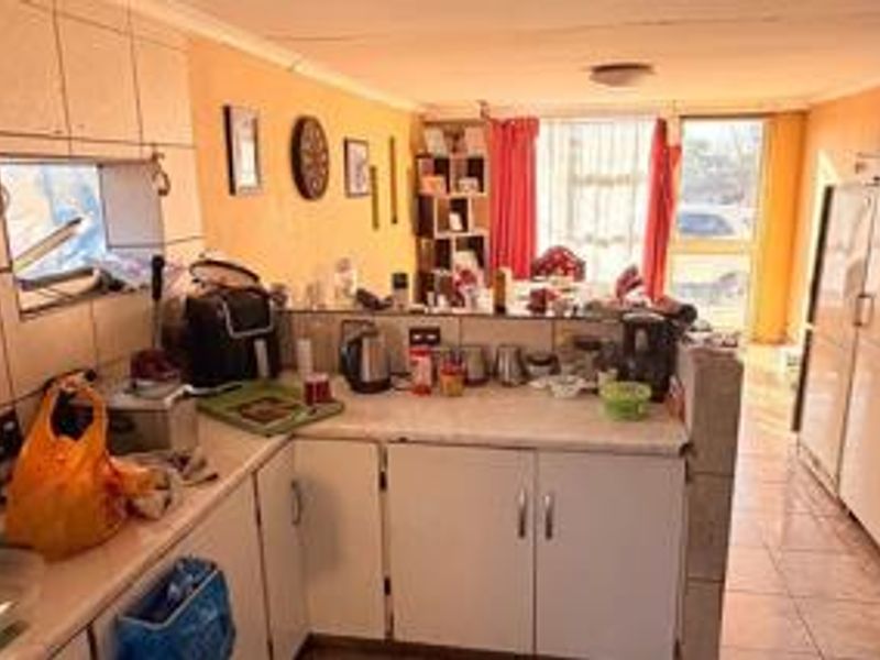 Open plan kitchen area featuring tiled splashbacks, laminate countertops, and built-in cabinetry, leading to a bright living space with sliding door access.