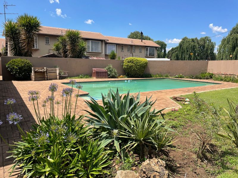 A private outdoor pool area featuring brick paving, a surrounding boundary wall, and established garden landscaping.