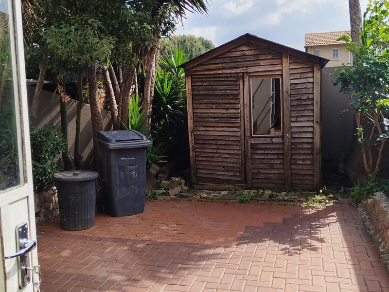 Rear exterior area featuring a paved patio and a weathered wooden garden shed, offering potential for outdoor landscaping or storage improvement.