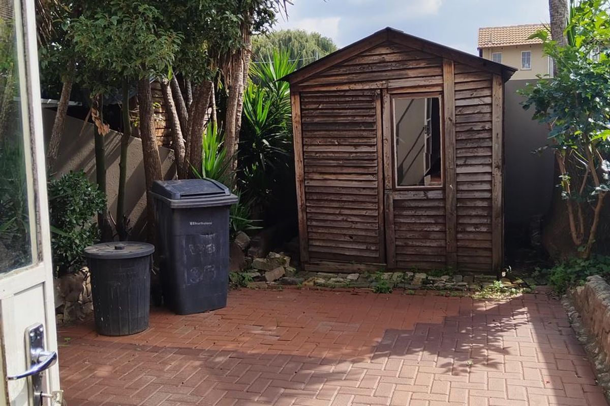 Rear exterior area featuring a paved patio and a weathered wooden garden shed, offering potential for outdoor landscaping or storage improvement.