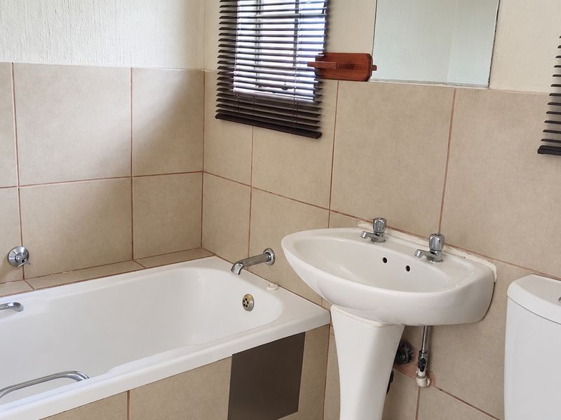 A functional bathroom featuring a pedestal basin, built-in bathtub, and toilet with neutral wall and floor tiling.