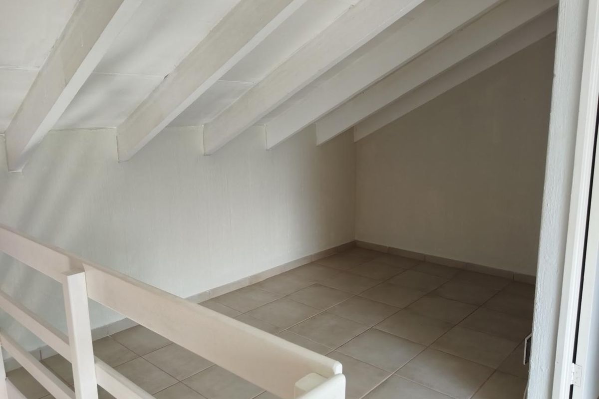 An empty attic-style bedroom featuring exposed white rafters, tiled flooring, and a protective wooden balustrade overlooking the lower level.