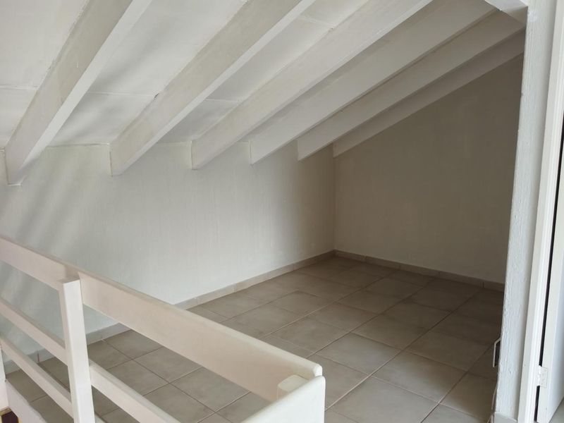 An empty attic-style bedroom featuring exposed white rafters, tiled flooring, and a protective wooden balustrade overlooking the lower level.