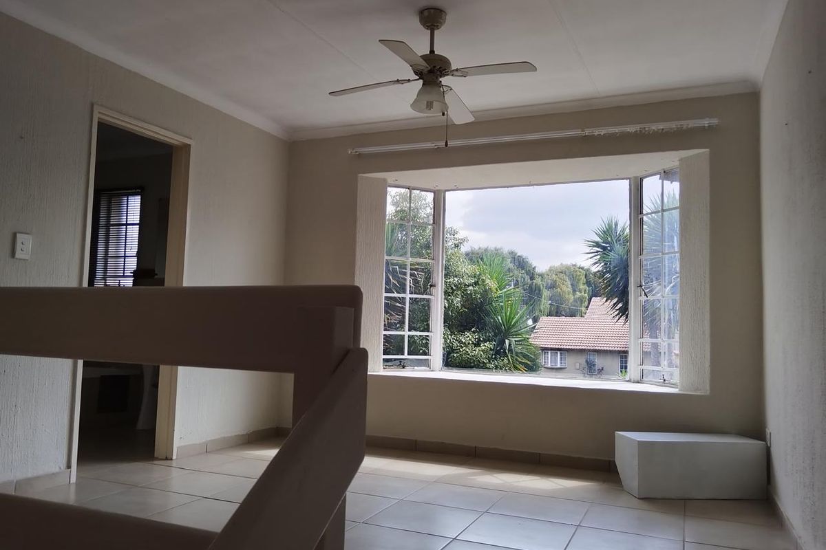 An empty living room featuring tiled flooring, a ceiling fan, and a large bay window with views of the surrounding greenery.