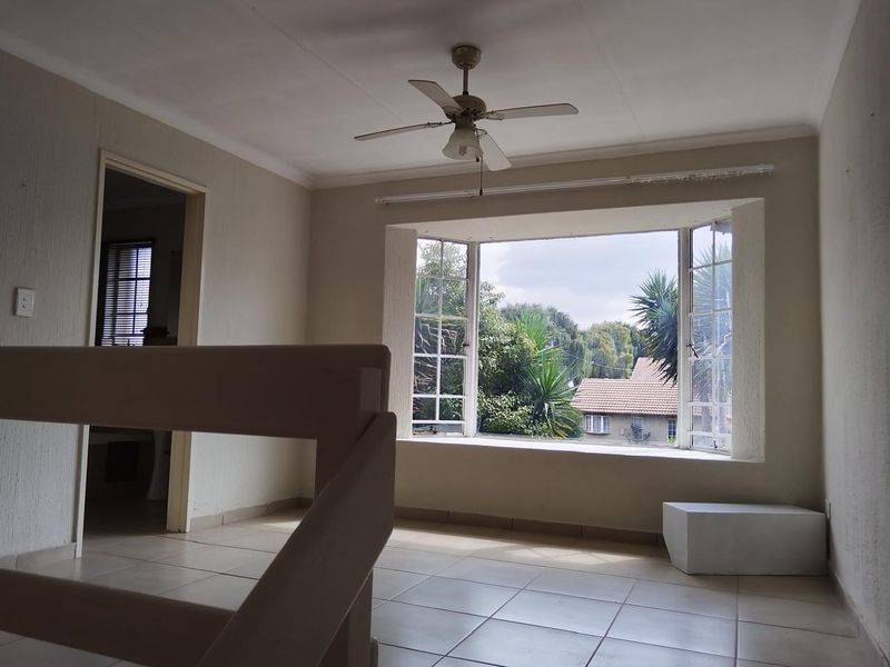 An empty living room featuring tiled flooring, a ceiling fan, and a large bay window with views of the surrounding greenery.