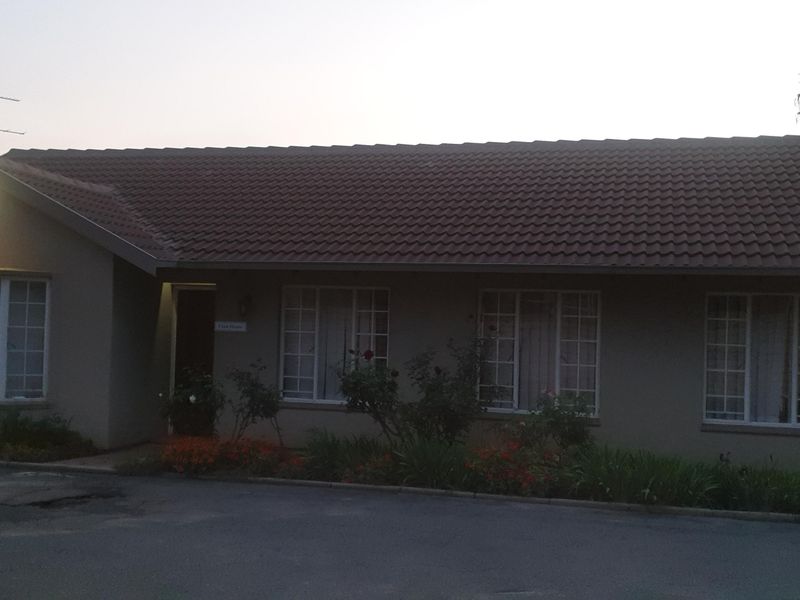 Front elevation of a single-story flat featuring a tiled roof, concrete driveway, and established garden beds.
