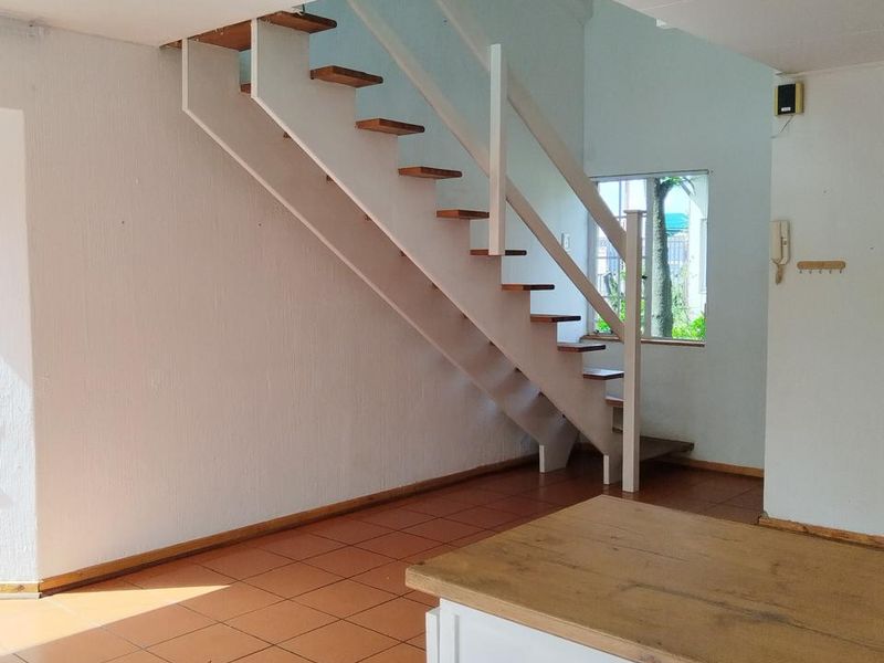 An open-plan living area featuring a staircase, tiled flooring, and built-in cabinetry, offering a blank canvas for interior design.
