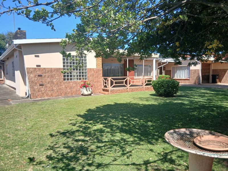 Rear view of the house featuring a covered patio, tiled facade accents, glass block window, and a spacious lawn area.