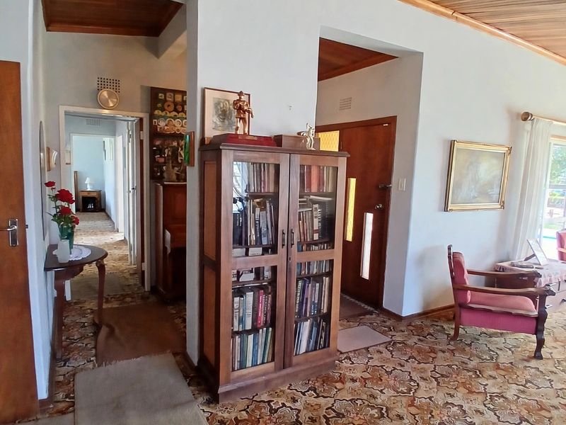 Living area featuring a timber tongue and groove ceiling, patterned carpeting, and traditional archway transitions leading to the hallway and entrance.