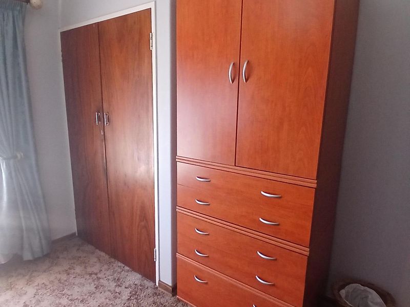 A bedroom featuring a built-in wooden cupboard, carpeted flooring, and coved ceiling details.