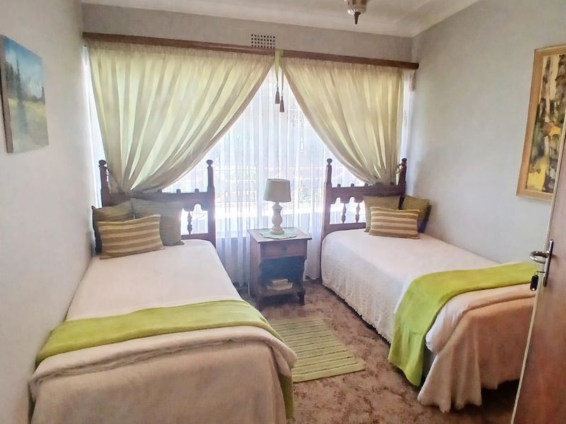 A bedroom featuring carpeted flooring, a central ceiling light fixture, and a window with curtains.