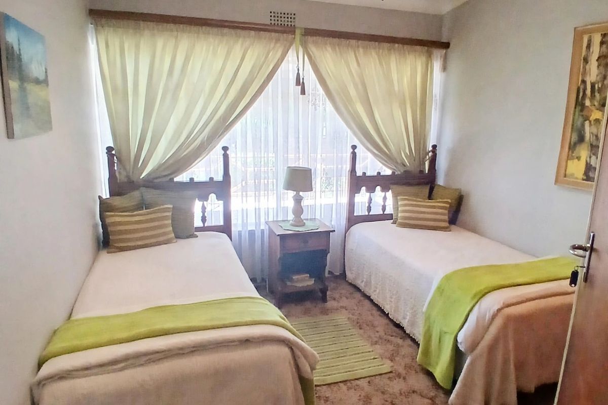 A bedroom featuring carpeted flooring, a central ceiling light fixture, and a window with curtains.
