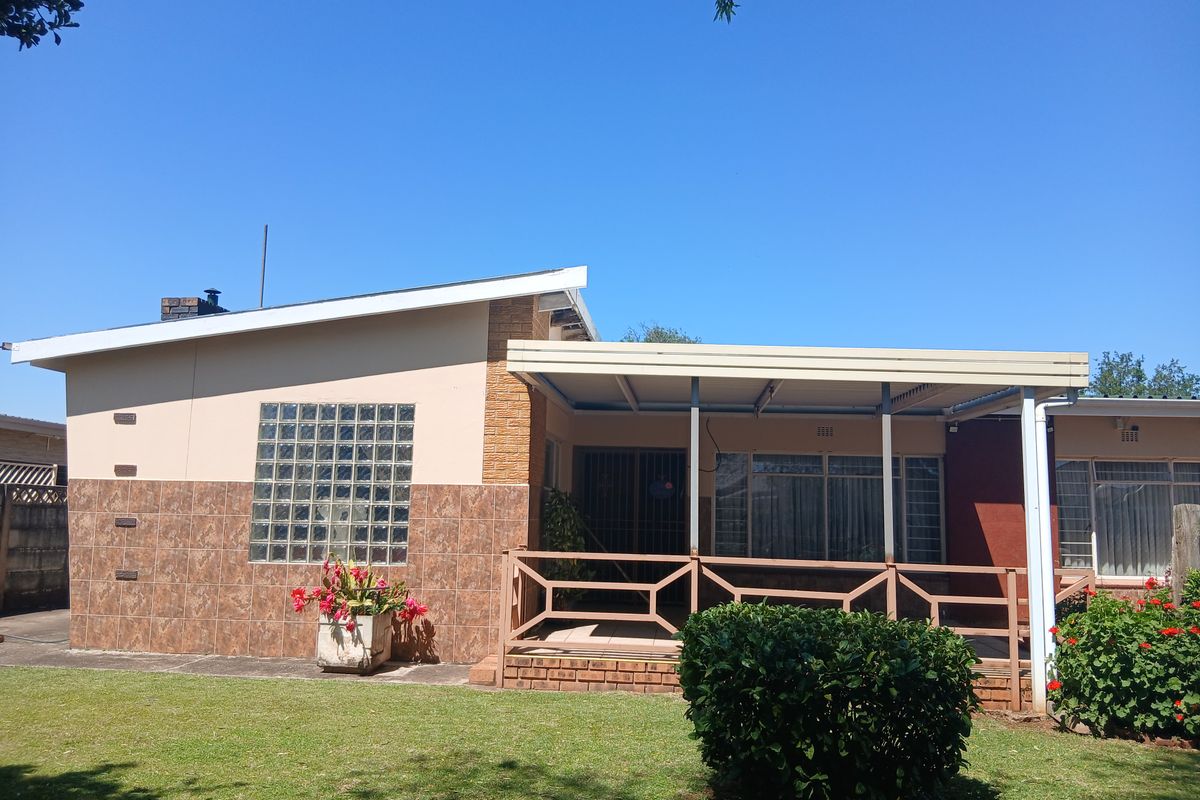 Rear view of the property featuring a covered patio area, glass block window detail, and a well-maintained garden space.