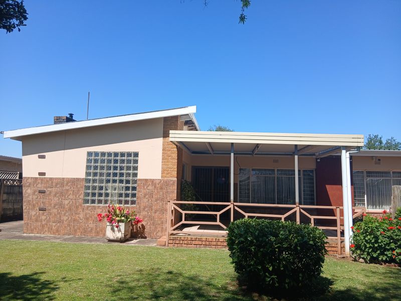 Rear view of the property featuring a covered patio area, glass block window detail, and a well-maintained garden space.