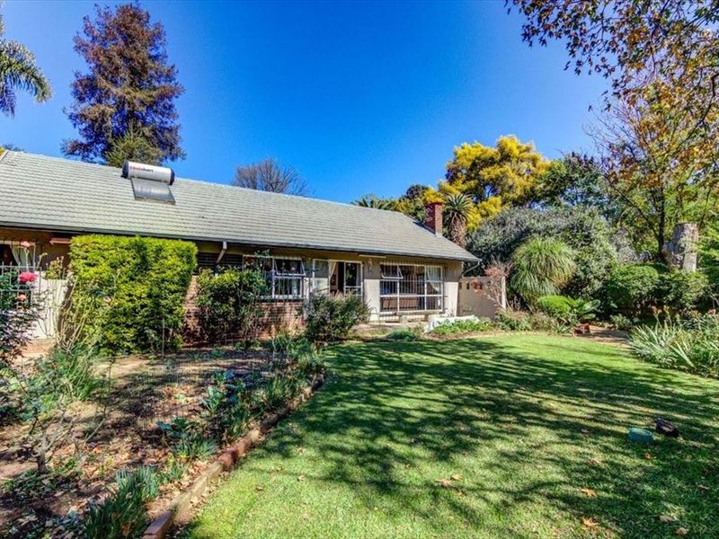 Rear view of the house featuring a brick facade, tiled roof with solar water heater, and a well-maintained garden area.