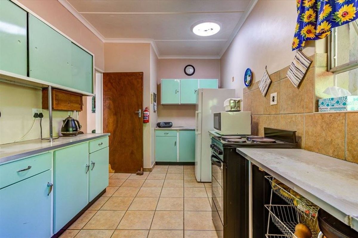 A functional kitchen featuring vintage-style cabinetry, tiled flooring, and a tiled backsplash, offering a dated aesthetic with potential for modern renovation.