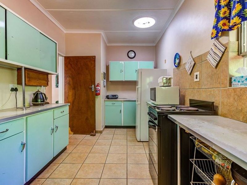 A functional kitchen featuring vintage-style cabinetry, tiled flooring, and a tiled backsplash, offering a dated aesthetic with potential for modern renovation.