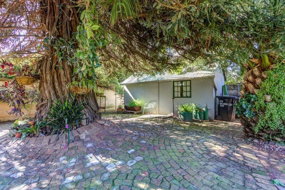 A rear garden area featuring mature trees, cobblestone paving, and a detached outbuilding structure.
