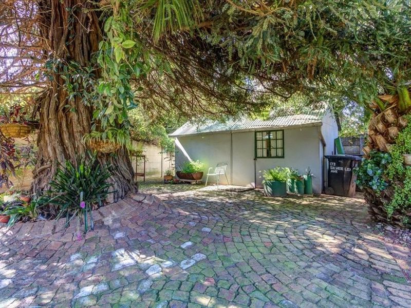 A rear garden area featuring mature trees, cobblestone paving, and a detached outbuilding structure.
