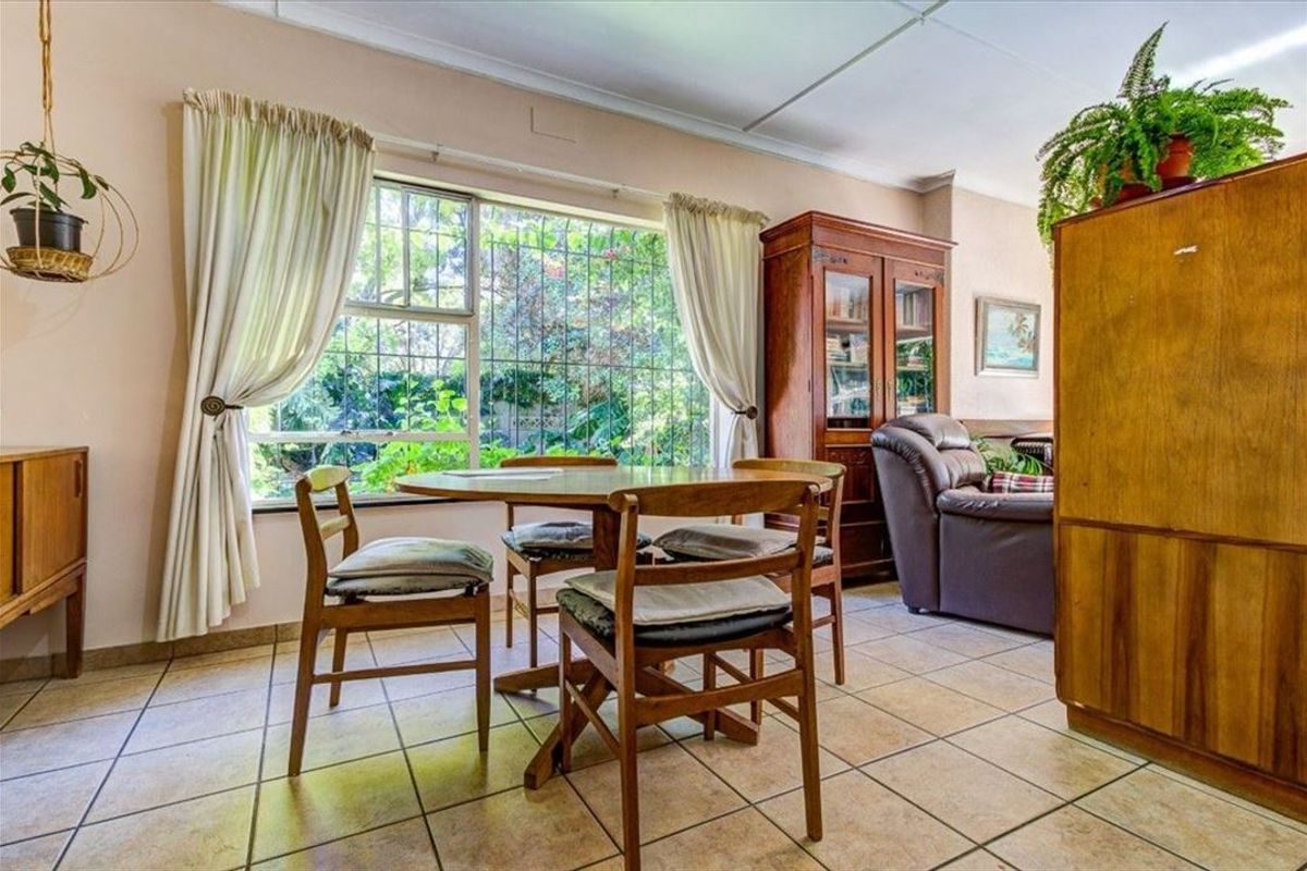 A living area featuring tiled flooring and a large window with security bars, offering a view of the garden.