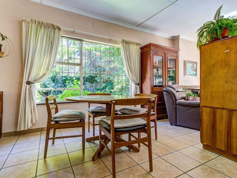 A living area featuring tiled flooring and a large window with security bars, offering a view of the garden.