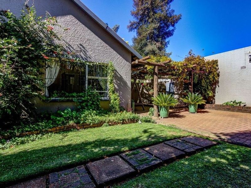 A private rear garden featuring a paved patio area, a timber pergola, and a stone pathway set within a landscaped lawn.