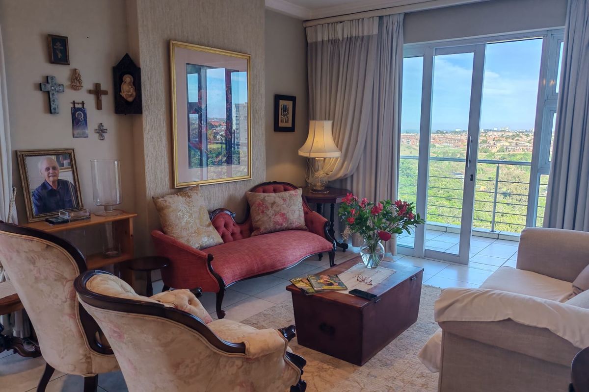 A comfortable living room featuring tiled floors, a textured feature wall, and large sliding glass doors that open onto a balcony with scenic views.