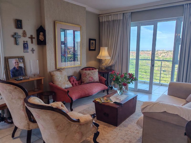 A comfortable living room featuring tiled floors, a textured feature wall, and large sliding glass doors that open onto a balcony with scenic views.