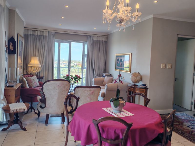 Spacious open-plan living and dining area featuring tiled floors, recessed lighting, a decorative chandelier, and large sliding doors leading to a balcony.