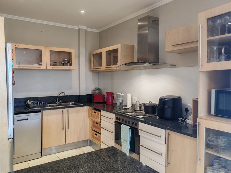 A functional kitchen featuring light wood cabinetry, dark granite countertops, stainless steel appliances, and a built-in oven with an extractor fan.
