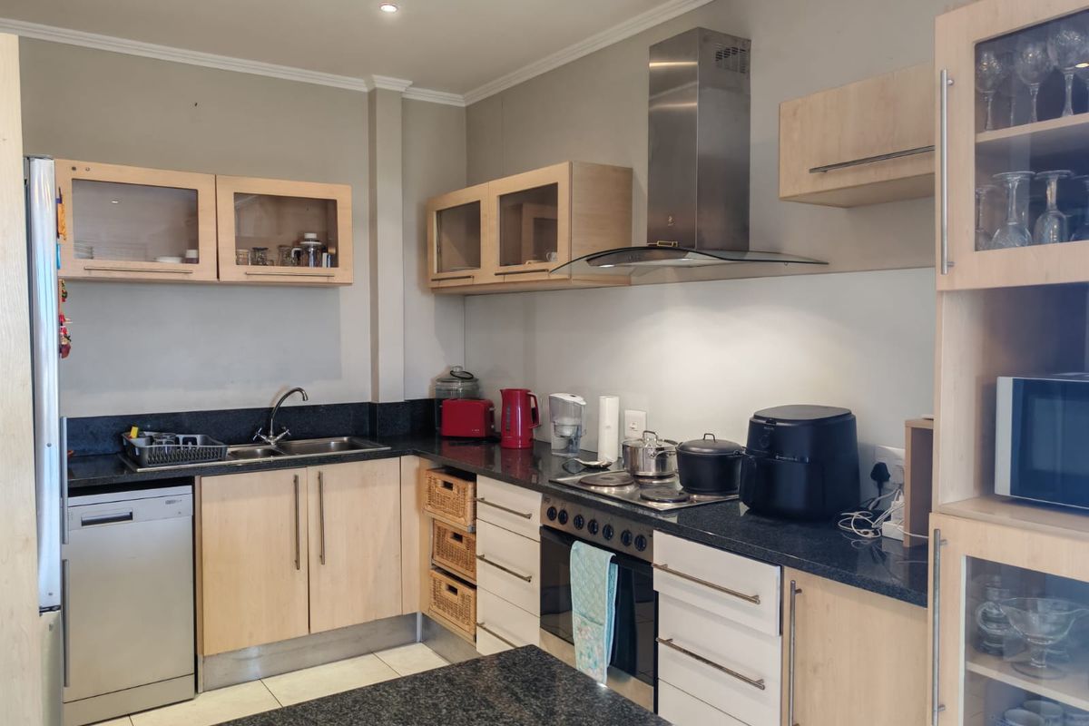 A functional kitchen featuring light wood cabinetry, dark granite countertops, stainless steel appliances, and a built-in oven with an extractor fan.