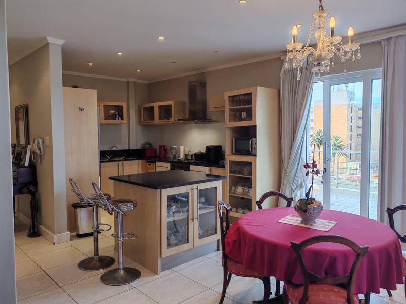 Open-plan kitchen and dining area featuring a central island with granite countertops, light wood cabinetry, and direct access to a private balcony.