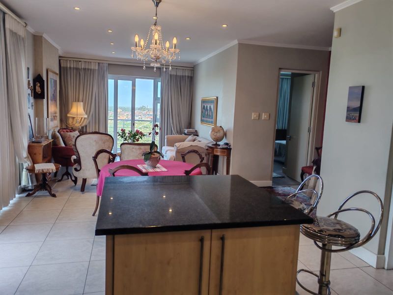 Spacious open-plan living and dining area featuring a central kitchen island, elegant chandelier lighting, and large sliding doors leading to a balcony with views.