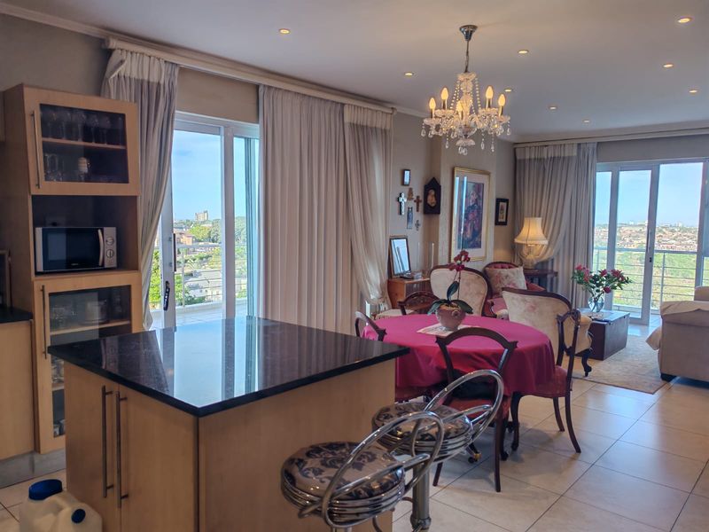 Spacious open-plan living and dining area featuring a granite-topped kitchen island, elegant chandelier lighting, and large sliding doors leading to a balcony with views.