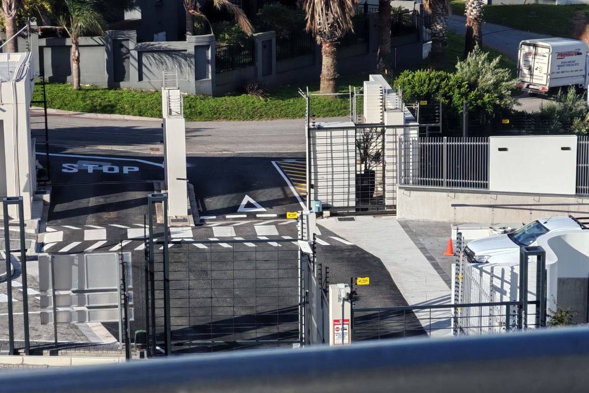 An elevated view of the apartment complex entrance featuring a secure gated access point with electric fencing and paved driveway.
