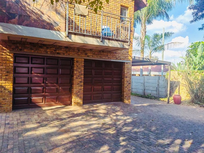 Front exterior view featuring a double garage with dark wood-look doors, a paved driveway, and an upper-level balcony with metal railings.