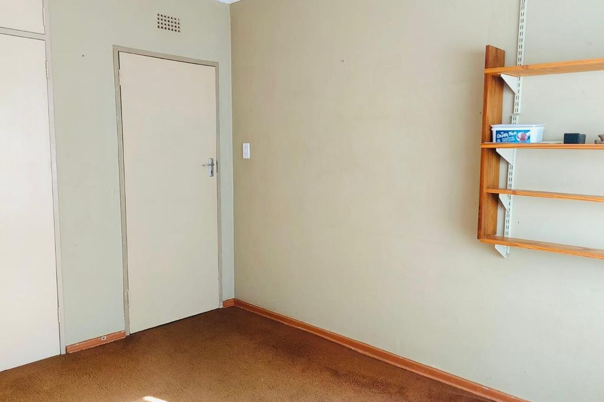 A vacant bedroom featuring built-in cupboard storage, wall-mounted shelving, and carpeted flooring, presenting a blank canvas for potential updates.