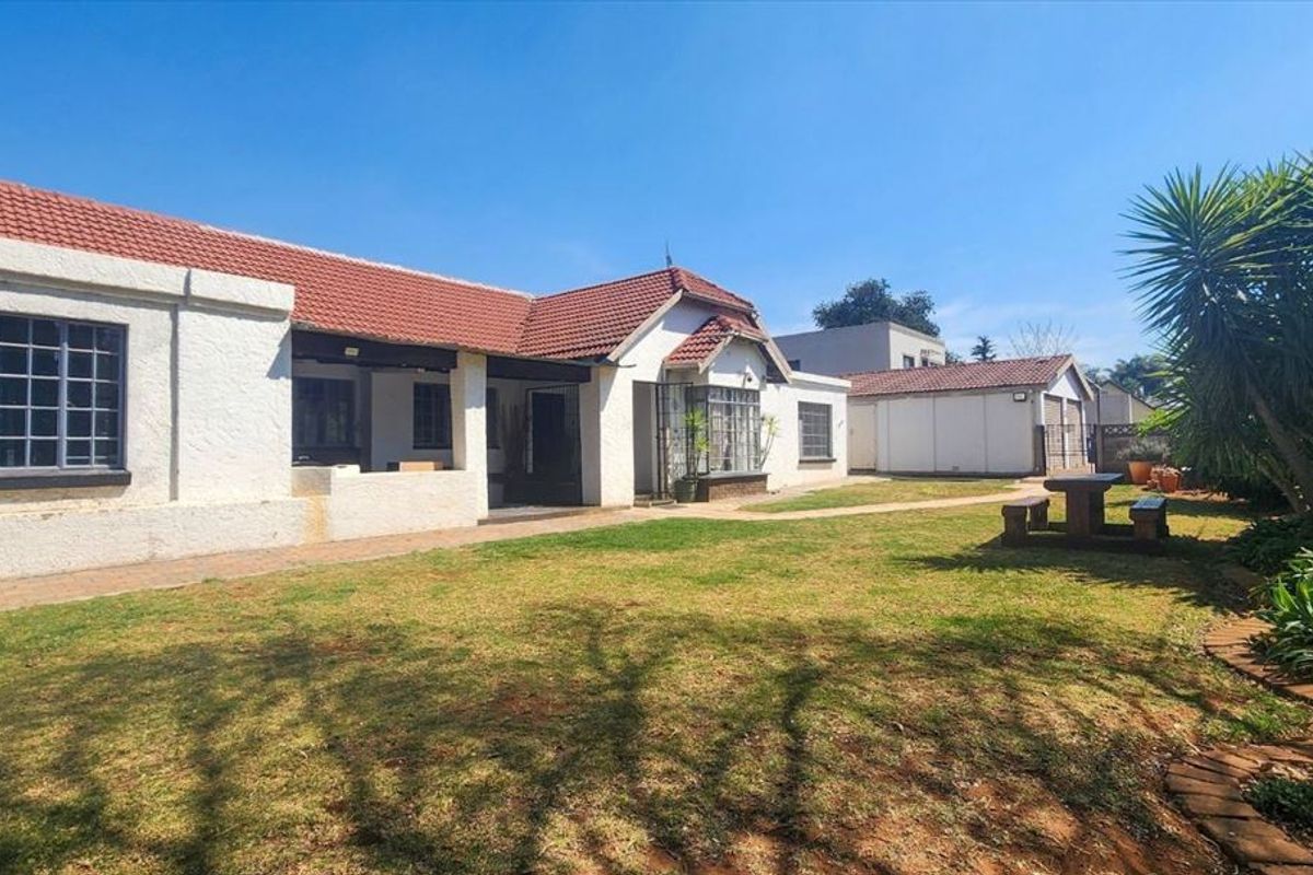 Rear view of the house featuring a tiled roof, paved walkway, and a spacious lawn area with an adjacent garage structure.