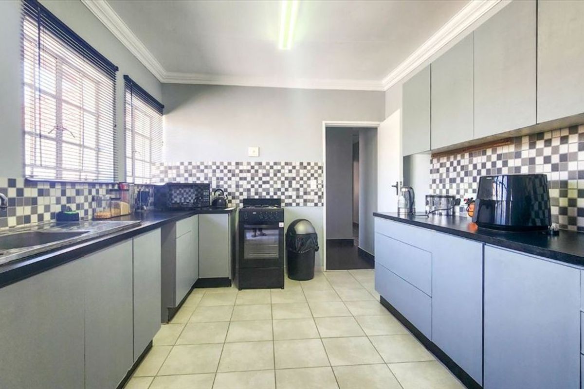 Functional kitchen featuring grey cabinetry, dark laminate countertops, a tiled backsplash, and ceramic floor tiles, providing a practical workspace with ample storage.
